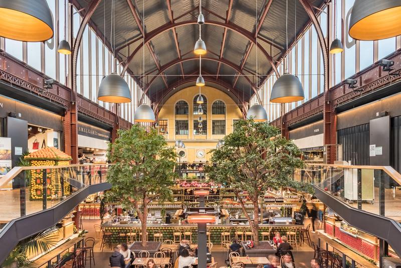Das Bild zeigt das Innere einer großen Bahnhofshalle mit Gastronomie